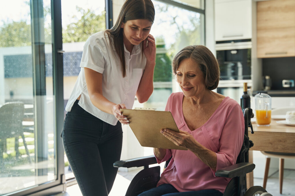 Woman signing documents in a mobility wheelchair, with her daughter assisting her.